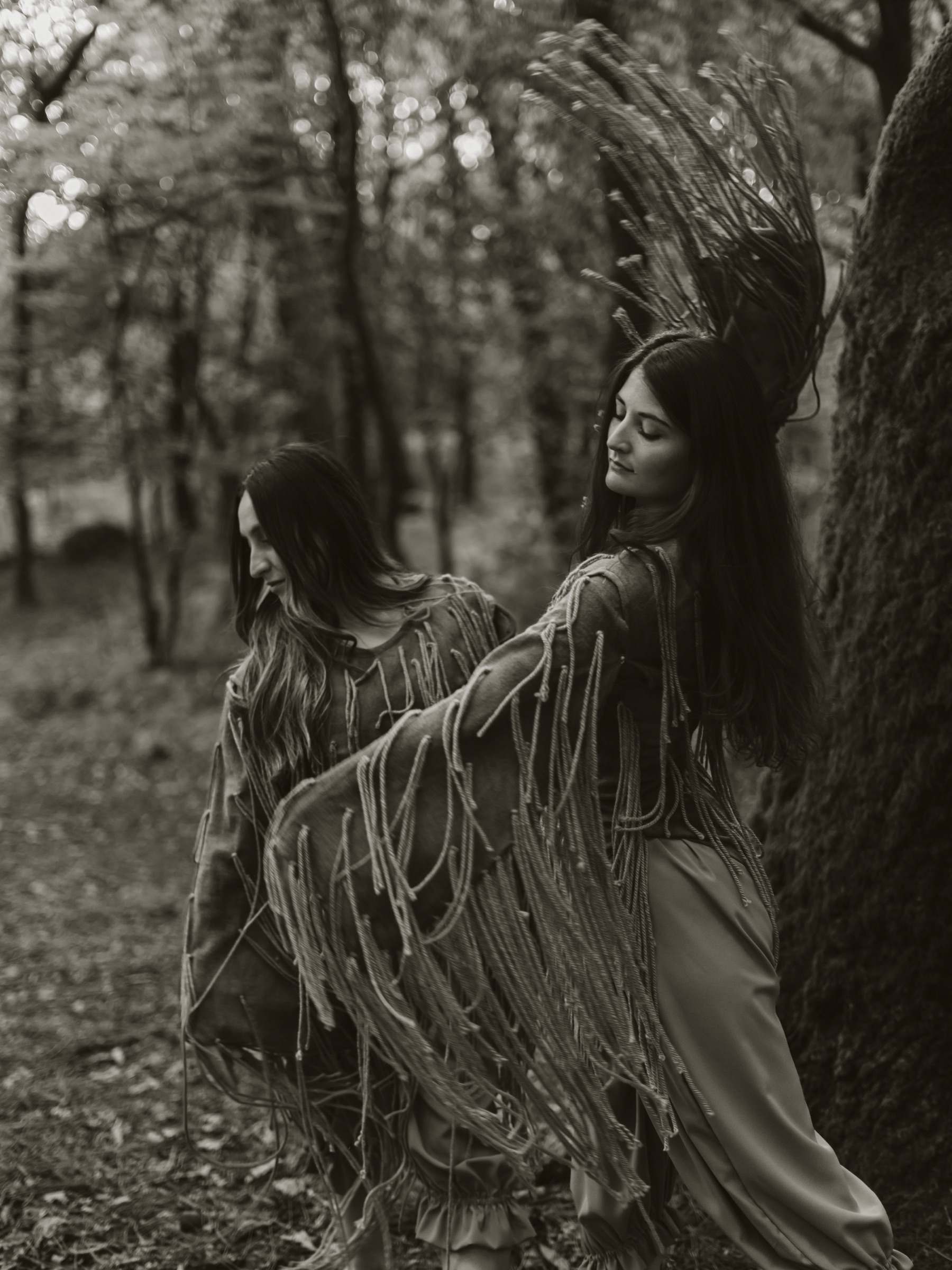 Dúas bailarinas con traxes de cordas movéndose no bosque, en branco e negro, en "Erguerse"