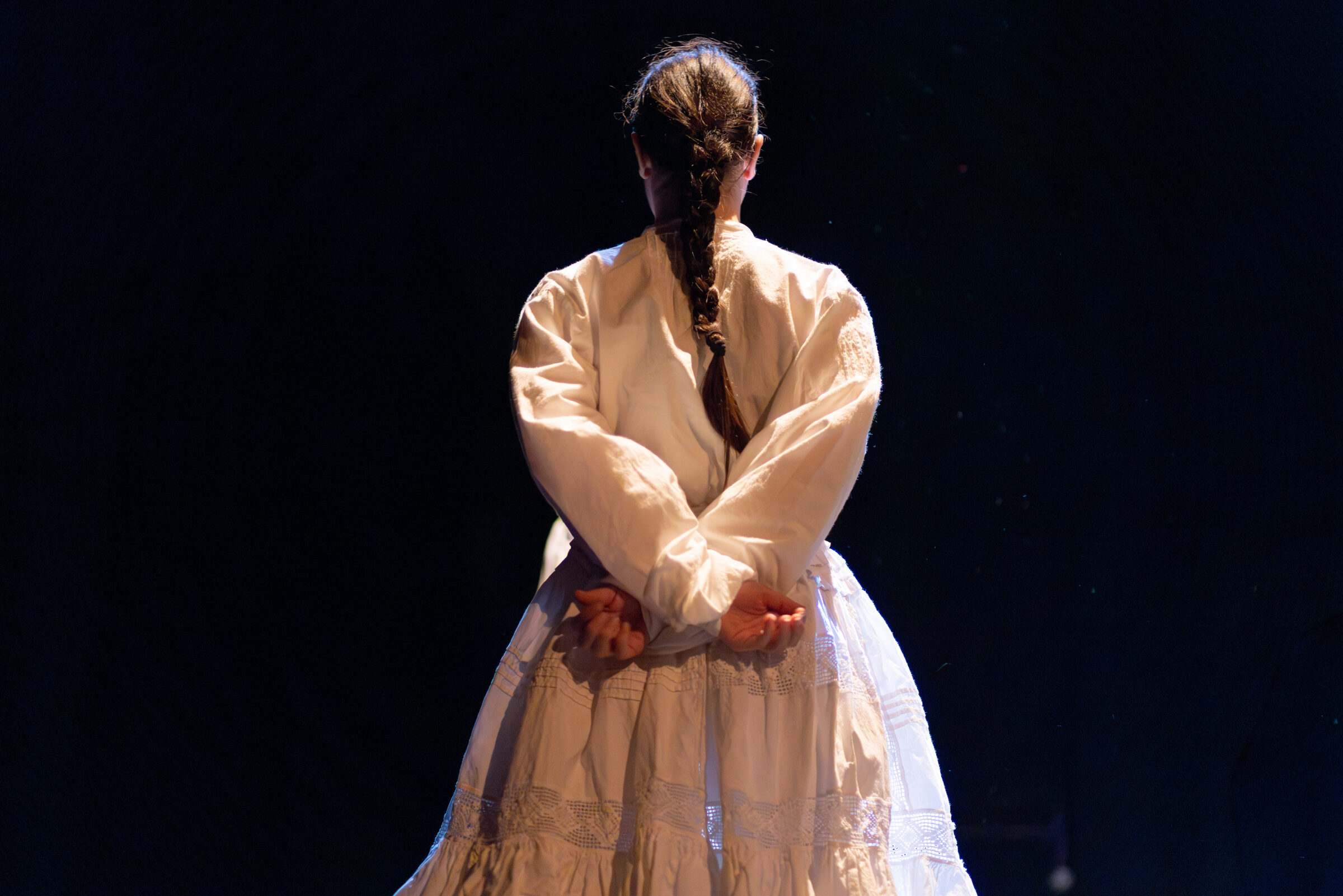 Bailarina de costas con camisa branca e trenza, mans nas costas