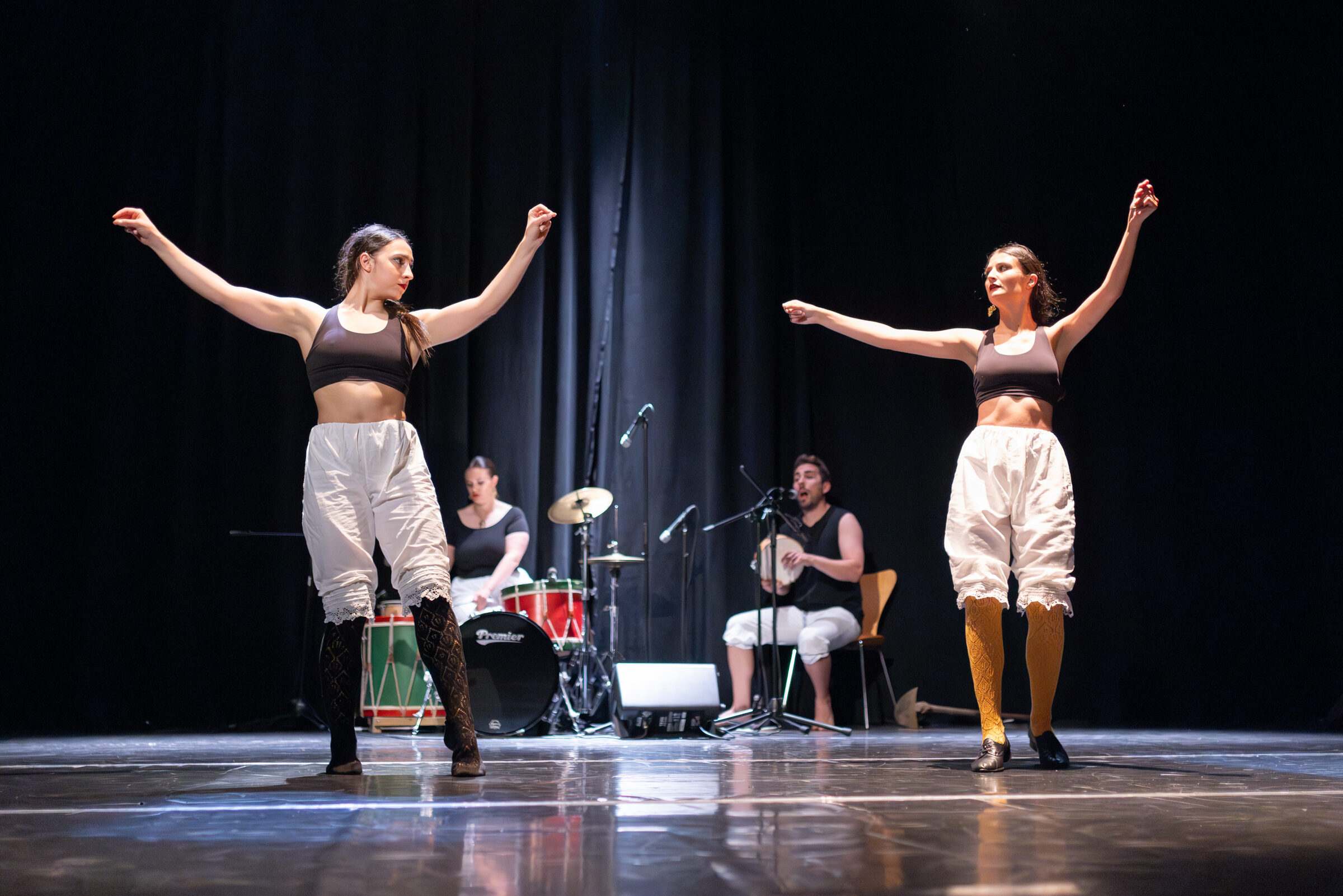 Dúas bailarinas cos brazos abertos e a banda de percusión detrás