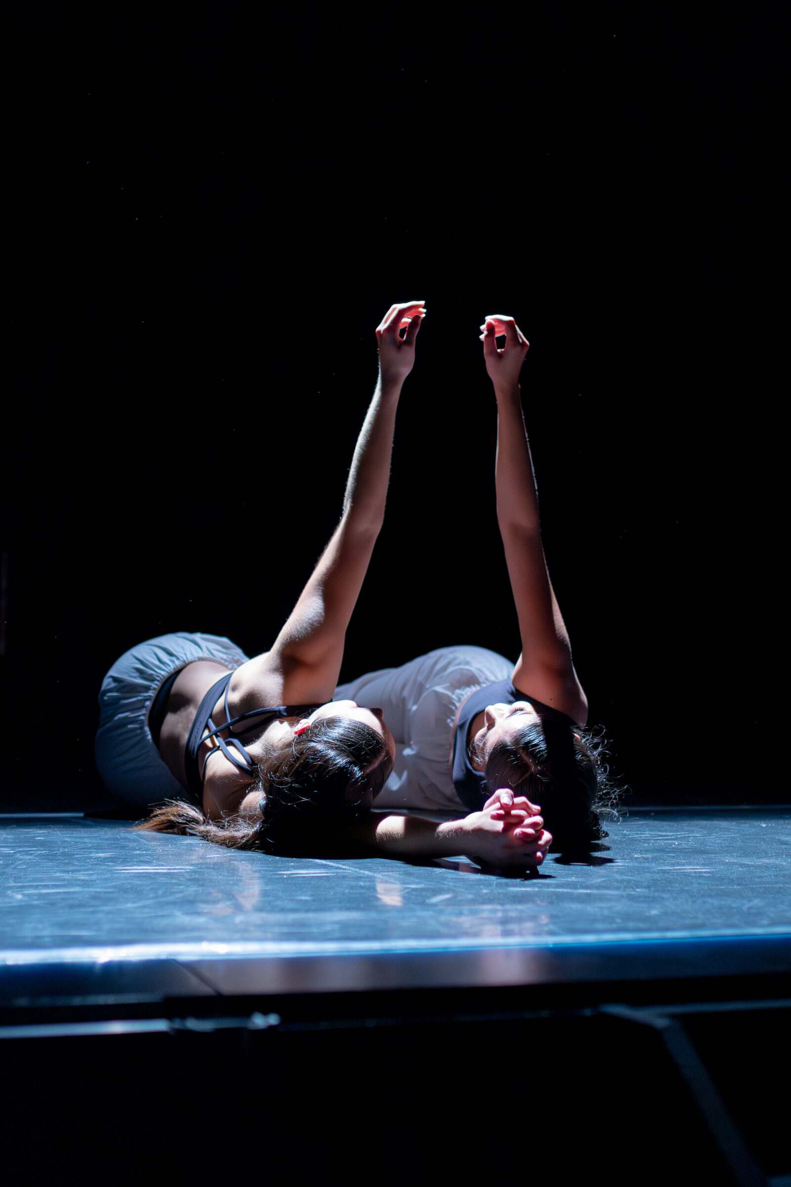 Bailarinas tendidas no chan cos brazos alzados baixo a luz