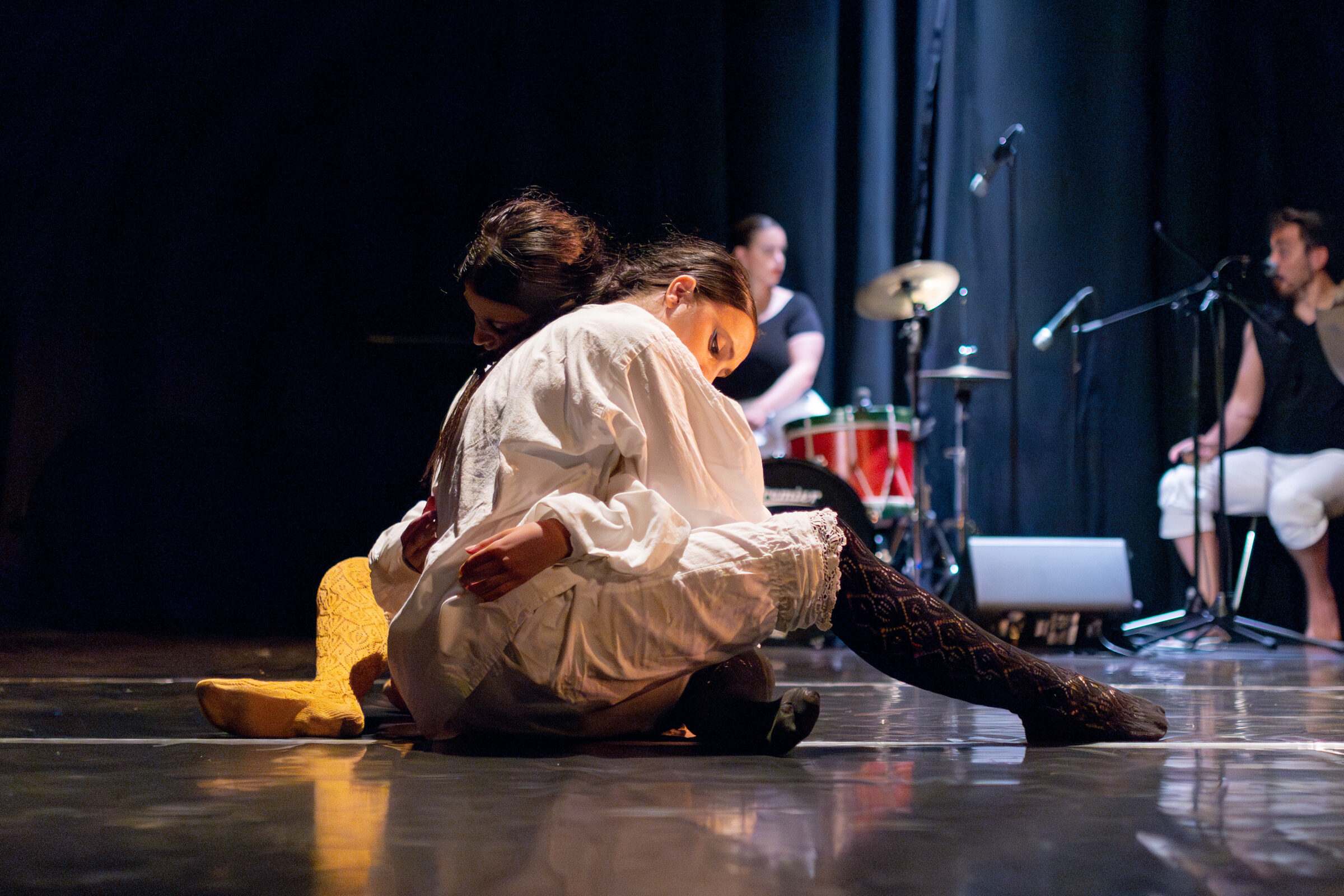 Bailarinas en movemento no chan con músicos ao fondo